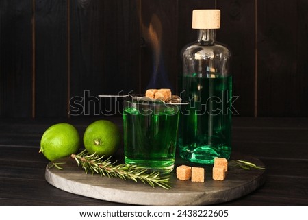 Absinthe in glass, flaming brown sugar, rosemary and lime on wooden table. Alcoholic drink