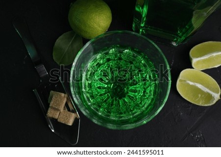 Absinthe in glass, spoon, brown sugar and lime on black table, flat lay. Alcoholic drink
