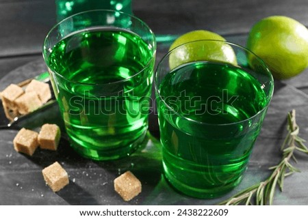 Absinthe in glasses, rosemary, brown sugar and lime on black wooden table, closeup. Alcoholic drink
