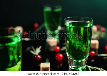 Absinthe in shot glass, cranberries and brown sugar on mirror table, closeup. Alcoholic drink
