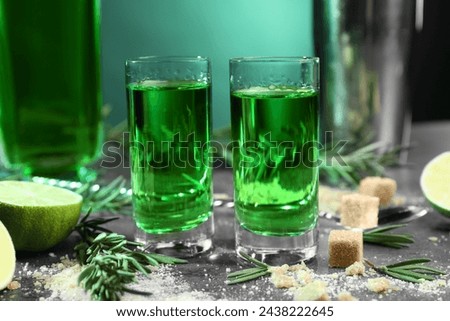 Absinthe in shot glasses, brown sugar, rosemary and lime on gray table, closeup. Alcoholic drink