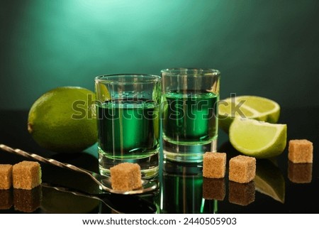 Absinthe in shot glasses, brown sugar, lime and spoon on mirror table. Alcoholic drink