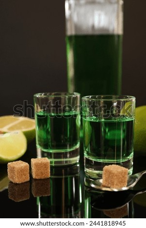 Absinthe in shot glasses, brown sugar, lime and spoon on mirror table. Alcoholic drink