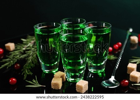 Absinthe in shot glasses, cranberries, rosemary and brown sugar on mirror table. Alcoholic drink