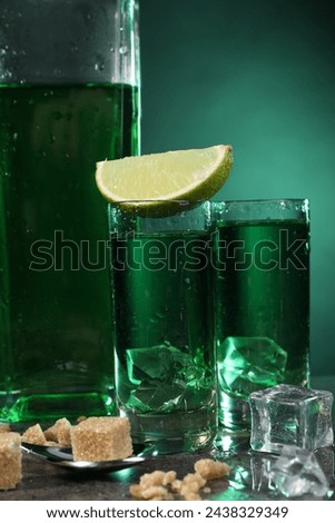 Absinthe in shot glasses with ice cubes, lime, brown sugar and spoon on gray table, closeup. Alcoholic drink