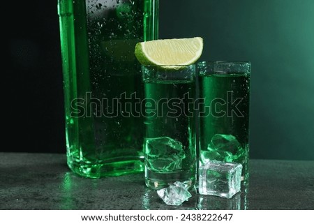 Absinthe in shot glasses with lime and ice cubes on gray textured table, closeup. Alcoholic drink