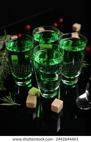 Absinthe in shot glasses, rosemary, brown sugar and spoon on mirror table. Alcoholic drink