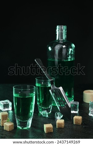 Absinthe in shot glasses, spoon, brown sugar and ice cubes on gray table against dark background. Alcoholic drink
