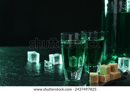 Absinthe in shot glasses, spoon, brown sugar and ice cubes on gray table against dark background, space for text. Alcoholic drink