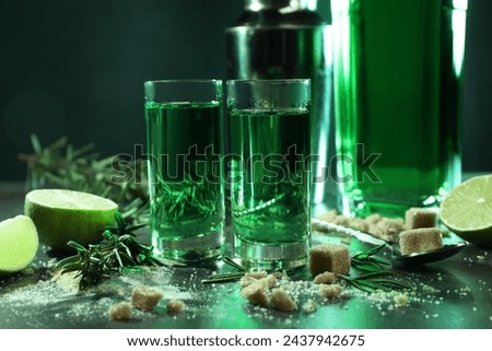 Absinthe in shot glasses, spoon, brown sugar, lime and rosemary on gray table, closeup. Alcoholic drink