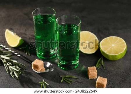 Absinthe in shot glasses, spoon, brown sugar, lime and rosemary on gray textured table, closeup. Alcoholic drink