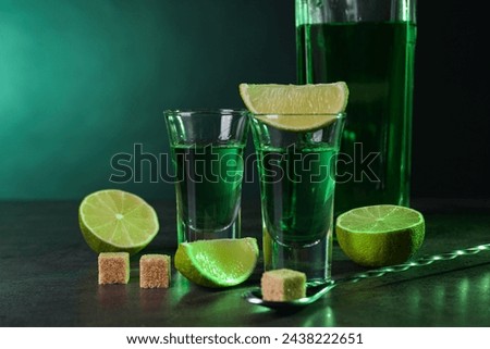 Absinthe in shot glasses, spoon, brown sugar cubes and lime on gray textured table against green background, space for text. Alcoholic drink