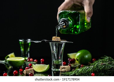 absinthe shots with sugar cubes. absinthe poured into a glass. bottle of absinthe with brown sugar, cranberries and lime, stainless steel spoon isolated on black background