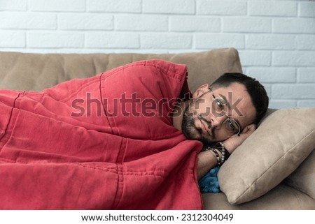 Absolute solitude. Side view of a depressed unhappy sad man lying on the sofa and hugging a blanket while feeling lonely, sad and miserable. Depression mental health social issue