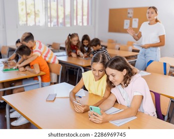 Absorbed interested preteen school children using mobile phones to watch game-based learning materials during lesson in classroom - Powered by Shutterstock