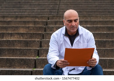 Absorbed Medical Doctor Or Dentist Sitting On Outdoor Stairs And Reading A Clinical Study Report