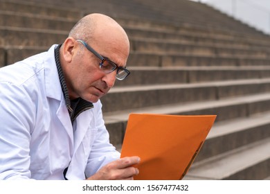 Absorbed Medical Doctor Or Dentist Sitting On Outdoor Stairs And Reading A Clinical Study Report