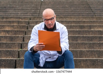 Absorbed Medical Doctor Or Dentist Sitting On Outdoor Stairs And Reading A Clinical Study Report