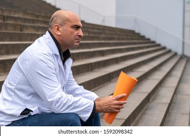 Absorbed Medical Doctor Or Dentist Sitting On Outdoor Stairs Holding A Clinical Study Report