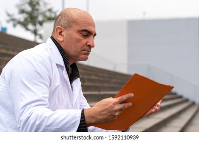 Absorbed Medical Doctor Or Dentist Sitting On Outdoor Stairs And Reading A Clinical Study Report