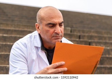 Absorbed Medical Doctor Or Dentist Sitting On Outdoor Stairs And Reading A Clinical Study Report