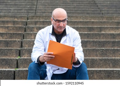 Absorbed Medical Doctor Or Dentist Sitting On Outdoor Stairs And Reading A Clinical Study Report