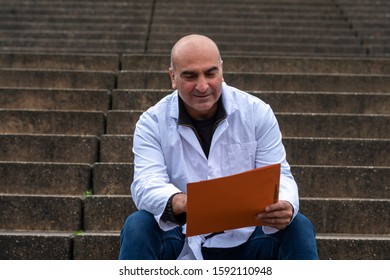 Absorbed Medical Doctor Or Dentist Sitting On Outdoor Stairs And Reading A Clinical Study Report