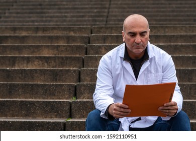 Absorbed Medical Doctor Or Dentist Sitting On Outdoor Stairs And Reading A Clinical Study Report