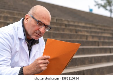 Absorbed Medical Doctor Or Dentist Sitting On Outdoor Stairs And Reading A Clinical Study Report