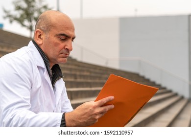 Absorbed Medical Doctor Or Dentist Sitting On Outdoor Stairs And Reading A Clinical Study Report