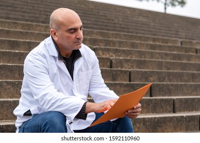 Absorbed Medical Doctor Or Dentist Sitting On Outdoor Stairs And Reading A Clinical Study Report