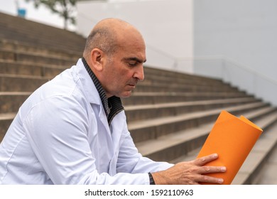 Absorbed Medical Doctor Or Dentist Sitting On Outdoor Stairs And Reading A Clinical Study Report