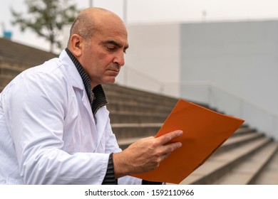 Absorbed Medical Doctor Or Dentist Sitting On Outdoor Stairs And Reading A Clinical Study Report