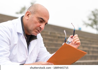 Absorbed Medical Doctor Or Dentist Sitting On Outdoor Stairs And Reading A Clinical Study Report