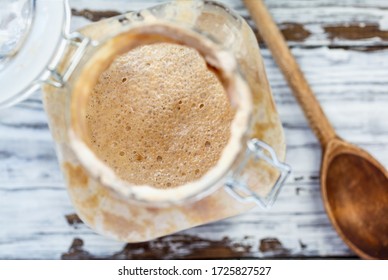 Abstract Of Active Live Whole Wheat Sourdough Starter With A Wooden Spoon Over A White Rustic Wood Table  Background With Free Space For Text Image Shot From Overhead View.