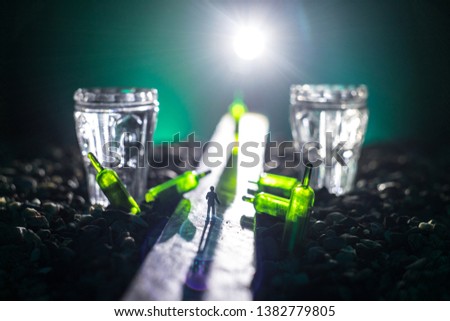 Abstract alcoholism concept. Silhouette of a man standing in the middle of the road on a misty night with giant glasses filled with alcoholic beverage. Creative artwork decoration