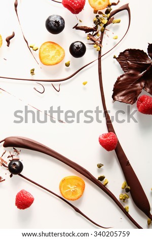 Abstract artistic chocolate swirl background with colorful candied kumquat, raspberries, blueberries pistachio nuts and chocolate coated leaves on white
