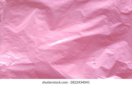 Abstract background featuring the surface texture of a soft pink crumpled plastic bag with natural folds and light reflections.