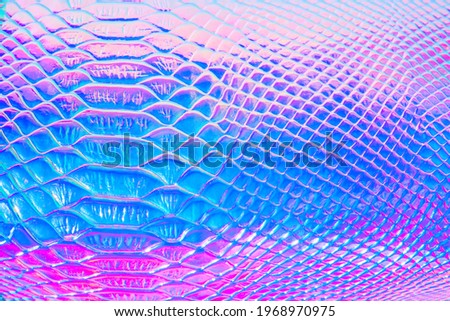Abstract background with holographic bright rainbow multicolor. Metallized macro close up. Imitation of rainbow color. Background with a reptile skin texture in pink and blue toned.
