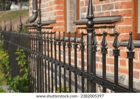 Abstract background of an iron black forged fence stretching into the distance and a brick wall of a house