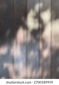 The abstract background is out of focus. Texture of a wooden floor exposed to tree leaf shadows, indicating natural activity outdoors.