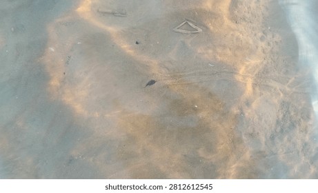 Abstract background of ripples and sand textures visible through clear flowing shallow ocean water at the beach.