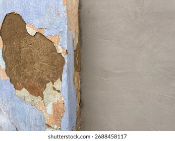 Abstract background texture featuring layers of peeling blue and orange paint over weathered plaster and stucco, contrasted with a smooth, unpainted beige wall, ideal for distressed surface concepts, 