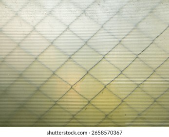 An abstract background texture of a translucent corrugated plastic sheet with the soft, shadowy pattern of a chain-link fence behind it. A minimalist and modern geometric design.