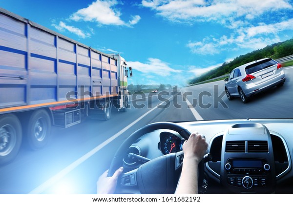 Abstract\
background with a truck with a trailer, car steering wheel and a\
silver family car against sky with blue\
lights