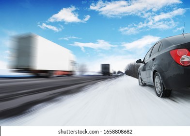 Abstract Background With Two White Box Trucks In Motion And A Black Family Car On The Countryside Winter Road In Motion With Snow Against A Blue Sky With Clouds