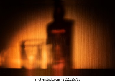 abstract background - yellow orange shadow from a bottle of brandy whiskey or rum on the wall . alcoholic drinks in a cozy atmosphere at the bar or at home. party and drinks