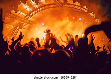 Abstract Blur Atmosphere: Happy People Enjoying Outdoor Music Festival Concert, Raised Up Hands And Clapping Of Pleasure, Active Night Life Concept, Play Of Light And Shadow On The Huge Stage