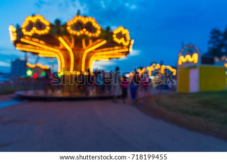Abstract Blur or Defocus Background image of People, Male Female and Kids, Walking around in Local Amusement Fun Park or Fun Fair in Thailand at Twilight.