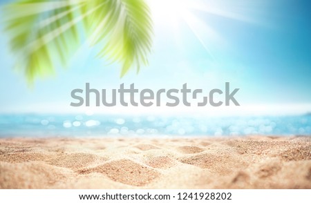 Abstract blur defocused background, nature of tropical summer beach with rays of sun light. Golden sand beach, sea water and palm leaves against sky. Copy space, summer vacation concept.